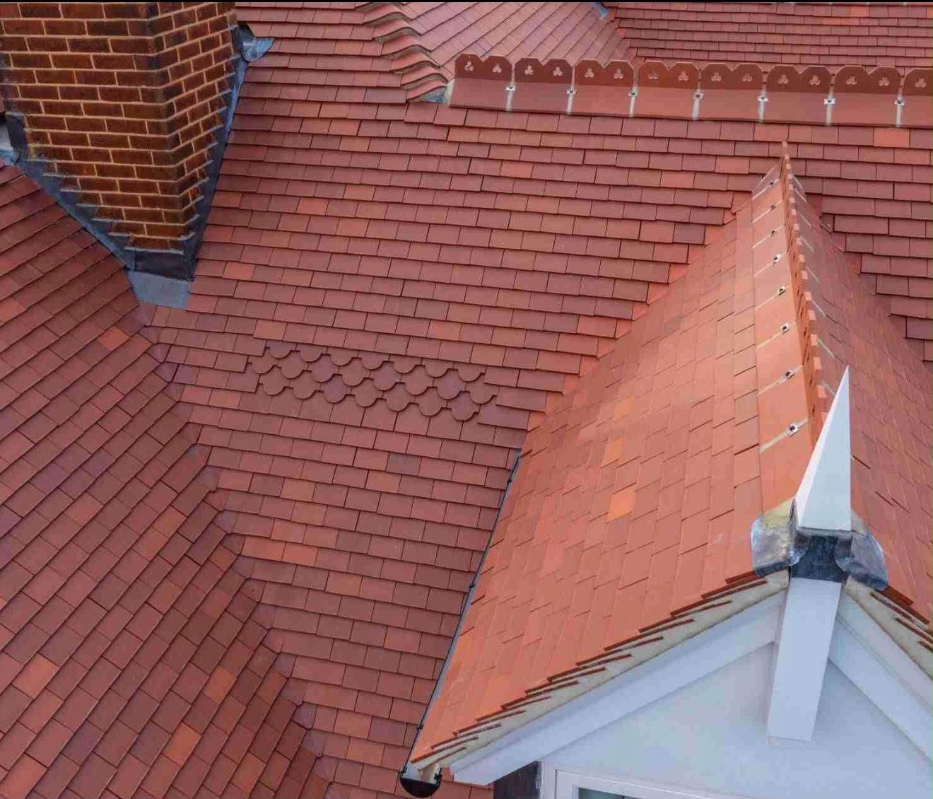 Close-up of natural terracotta clay roof tiles with decorative fan detailing and a pointed finial ridge