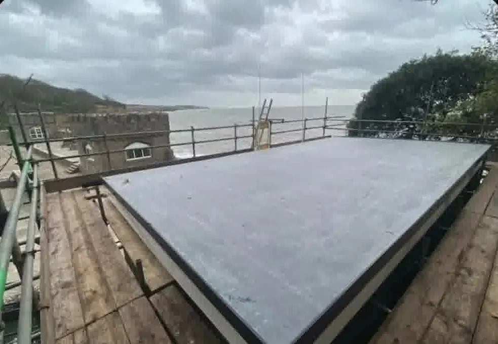 Grey EPDM rubber flat roof on scaffolding overlooking the sea