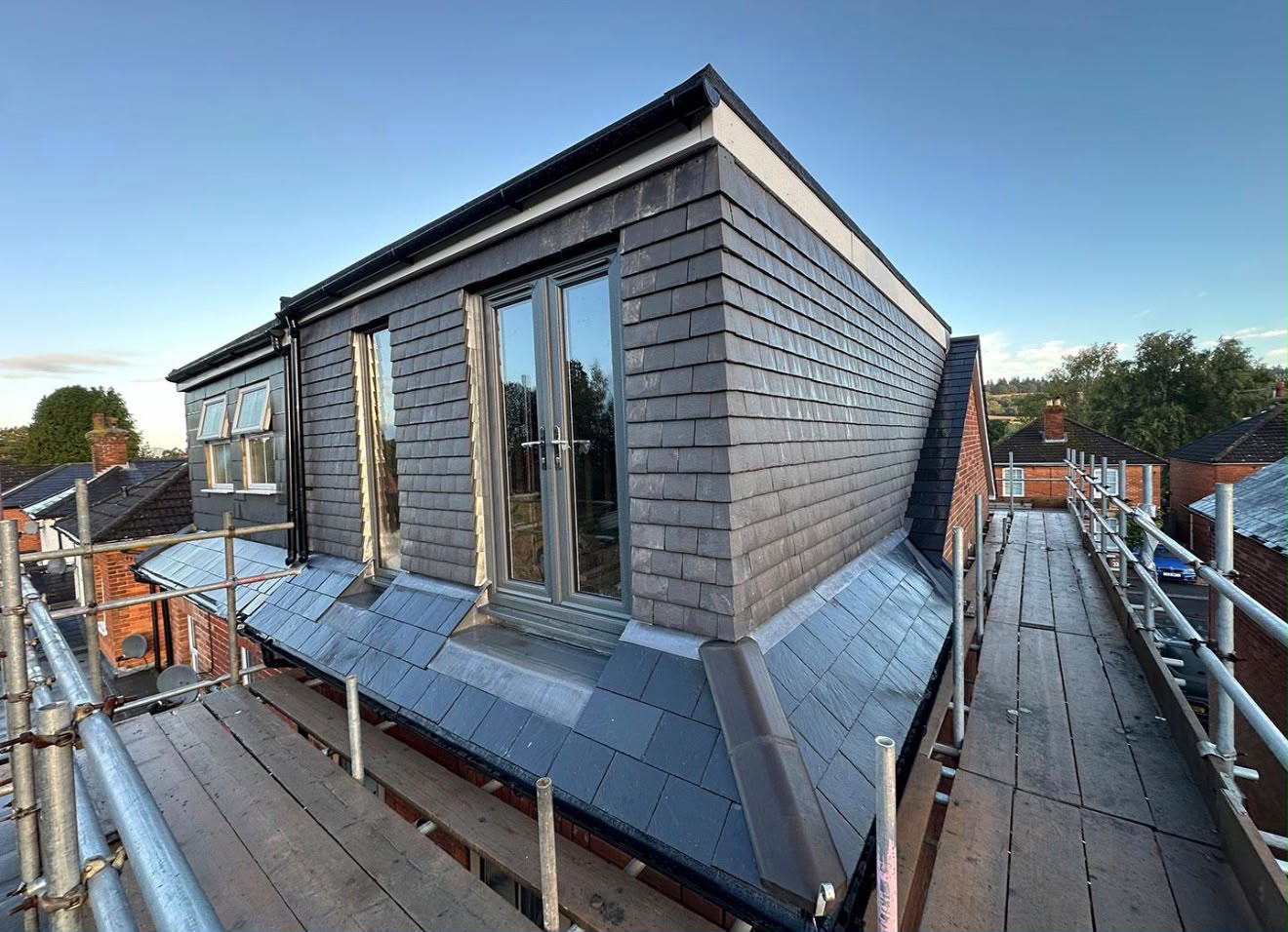 Newly built rear dormer clad in grey slate with grey-framed French doors on a scaffolded roof