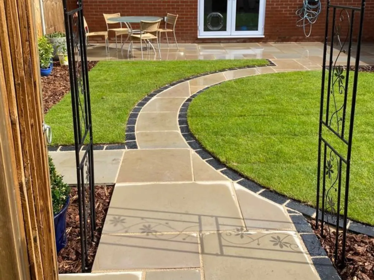 Curved sandstone path with dark edging leading through a lawn to a patio
