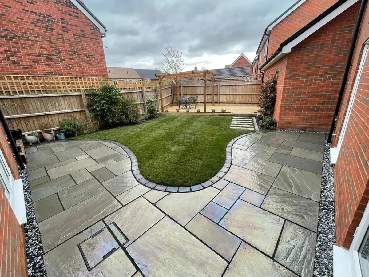 Landscaped garden with grey paving, curved lawn, fencing and a pergola over decking