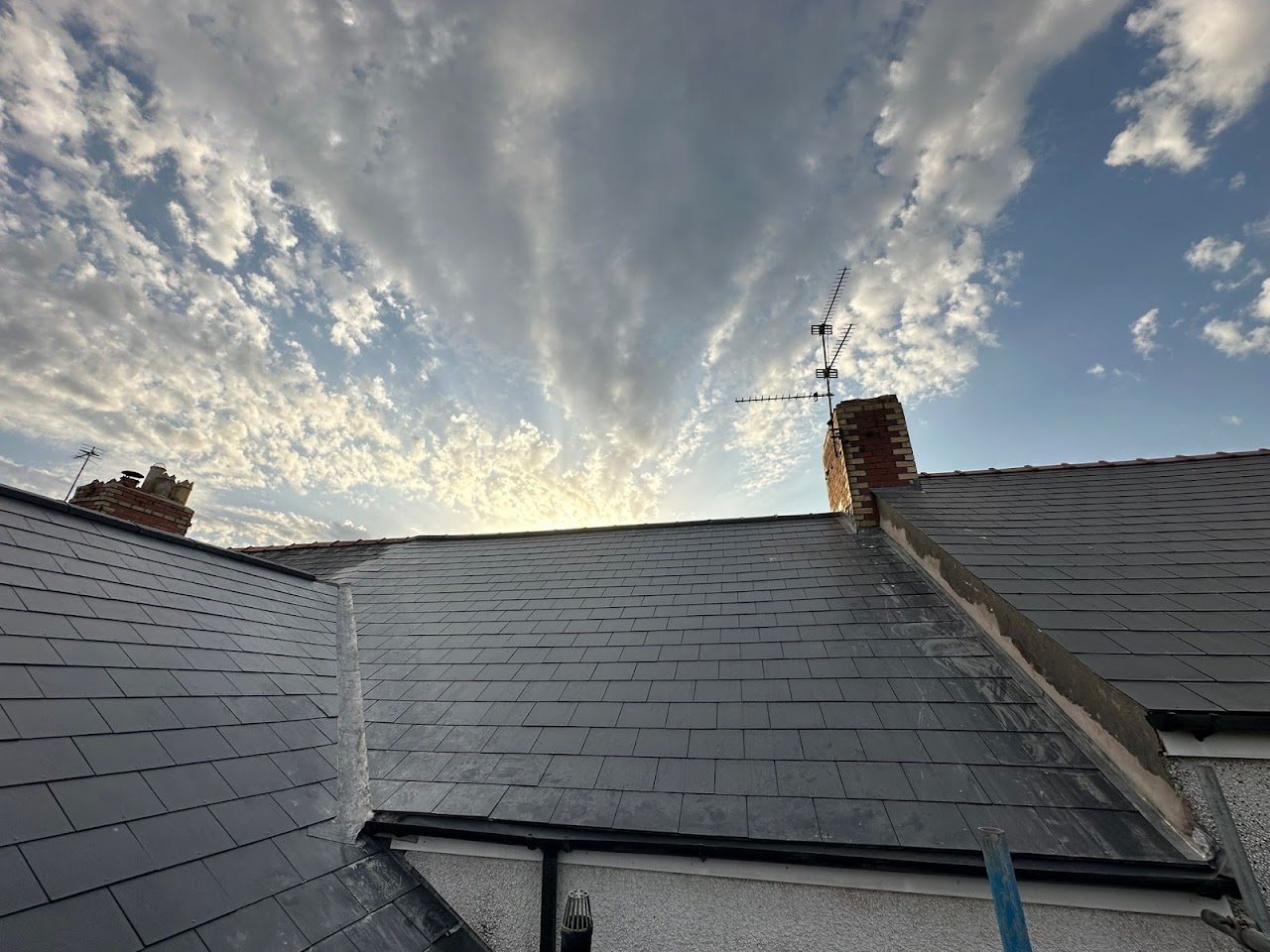 New slate roof with brick chimney under a dramatic sky